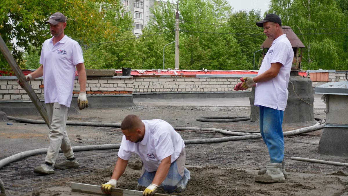 Team of construction workers pouring and leveling cement on a rooftop.